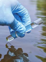 gloved hand dipping test tube into a water source