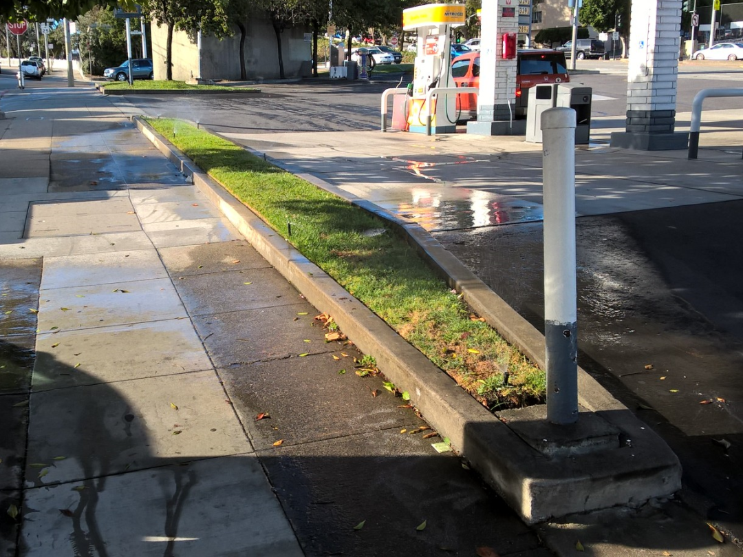 Small strip of grass being watered at a gas station.