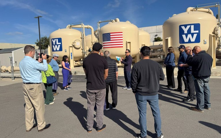 tour group stands in front of treatment plant, large beige tanks with YLWD logos and US flag