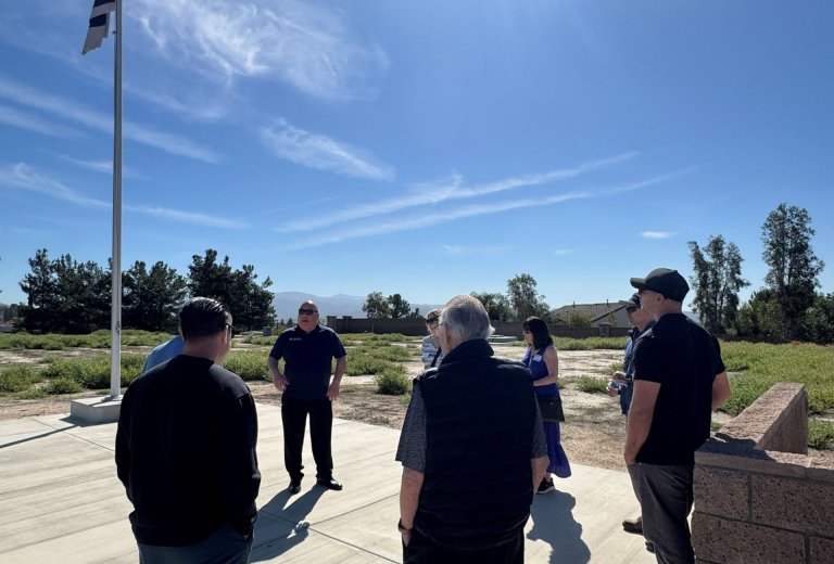 group of people gather under YLWD flagpole standing on concrete surrounded by grass and brick wall