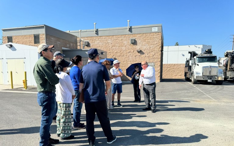 Group stands in front of brown building near sewer vactor truck in parking lot