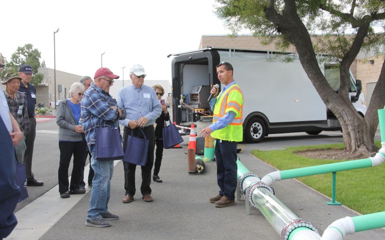 Maintenance worker presenting to group an above ground sewer pipeline demonstration. They are standing in front of a white inspection van.