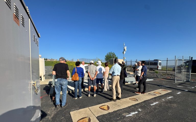 Group gathers on asphalt near grey electical box looking down through the ground