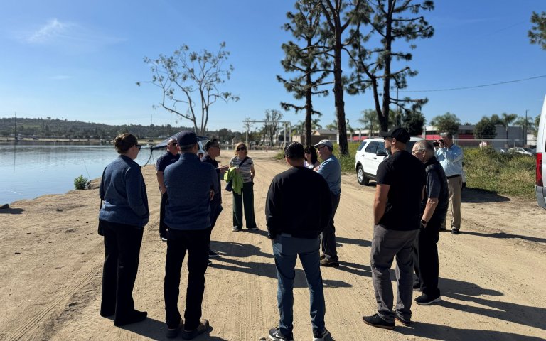 group of people standing on dirt near body of water