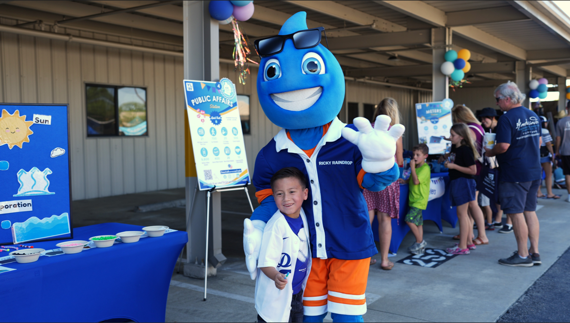 Photo captures a child smiling with a water drop mascot at an event.