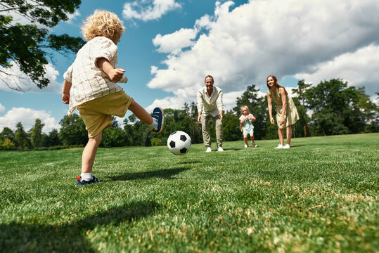 Child kicking a soccer ball at a park with family